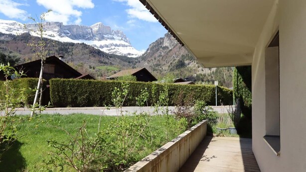 Une terrasse en bois menant à un bâtiment d’où l’on peut admirer la vue sur la montagne.