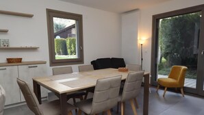 Un coin repas avec une table et des chaises en bois, une petite table d’appoint et une vue sur l’extérieur grâce à une porte coulissante.