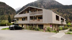 Un immeuble à plusieurs étages doté de balcons, d’un espace de stationnement et surplombant un paysage montagneux.