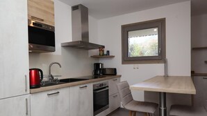 Une cuisine moderne équipée d’un four encastré, d’un four à micro-ondes et d’une hotte en acier inoxydable. On y trouve une table à manger avec deux chaises, et une fenêtre au-dessus.