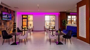 A modern dining area with a stone wall, a flat-screen TV, and a blue sofa. - Royal Elisa Annaba (Annaba)