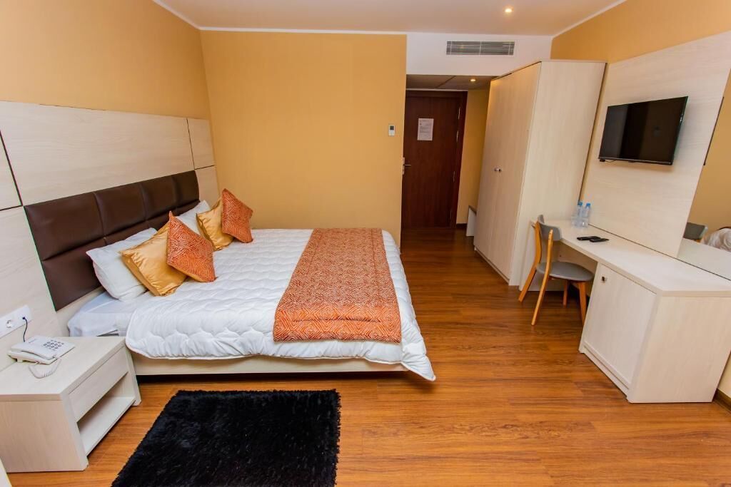 A hotel room with a bed, bedside table, TV, desk, and wardrobe.