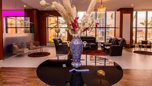 A modern lobby with a central round table, a decorative vase with flowers, leather sofas, and large windows offering views of the city. - Royal Elisa Annaba (Annaba)