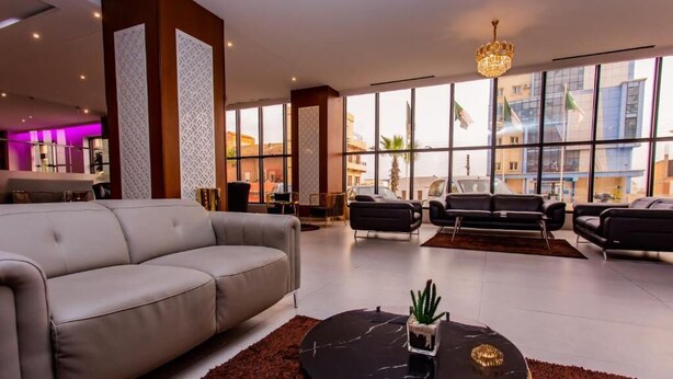 A modern hotel lobby with a grey sofa, black armchairs, and a round black coffee table with a cactus. - Royal Elisa Annaba (Annaba)