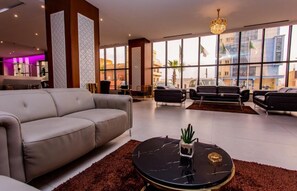 A modern hotel lobby with a grey sofa, black armchairs, and a round black coffee table with a cactus. - Royal Elisa Annaba (Annaba)