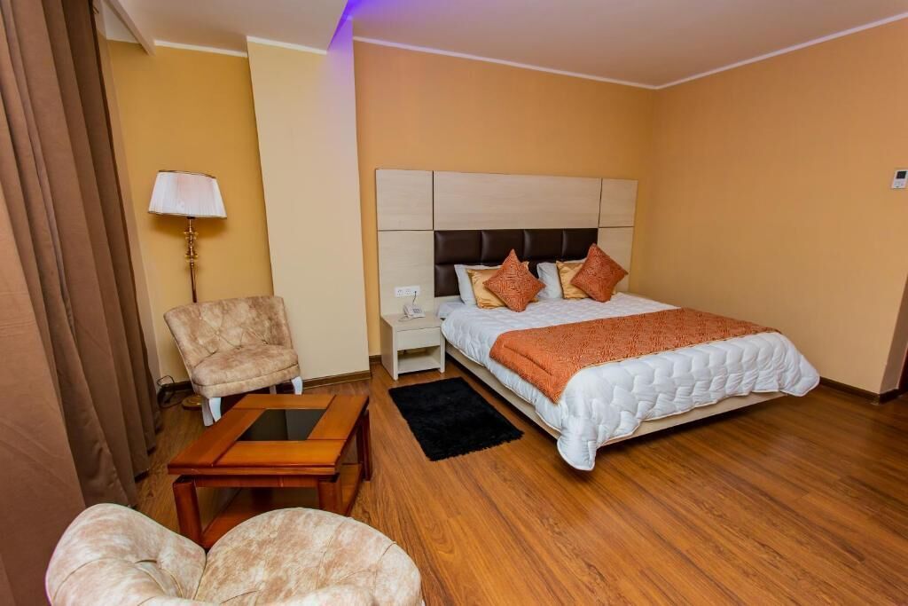 A hotel room with a bed, a nightstand, a lamp, a chair, and a small table.