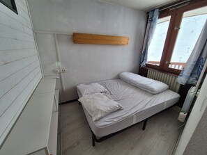 A small, single-bed room with a wooden shelf, a radiator, and a window with curtains. - La Mongie Apartment for 8 People, Right on the Slopes   (Bagnères-de-Bigorre)