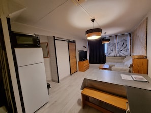 Kompakti oleskelutila, jossa on pieni keittiö, sohva, ruokapöytä ja televisio.