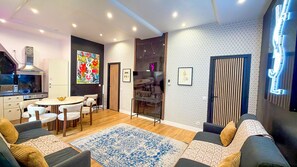 A modern living room with a sofa, a dining table, and chairs. There is a kitchen area with a stove and cabinets. The walls have patterned wallpaper and artwork. - Urban Flat 156 - Yves Flat in Montorgueil (París)