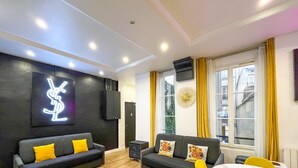 A modern living room with two sofas, a large window with yellow curtains, and a wall-mounted speaker. - Urban Flat 156 - Yves Flat in Montorgueil (París)