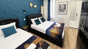 A hotel room with two beds, a blue geometric wall, a framed picture of the Eiffel Tower, and a bathroom with a glass shower. - Urban Flat 156 - Yves Flat in Montorgueil (París)