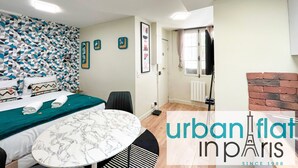 A modern bedroom with a patterned wall, a bed with neatly folded towels, a marble table, and a brick fireplace. - Urban Flat 162 - Charming Studio in Montorgueil (París)