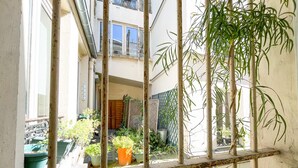 A courtyard with potted plants, a metal gate, and a building with windows in the background. - Urban Flat 162 - Charming Studio in Montorgueil (París)