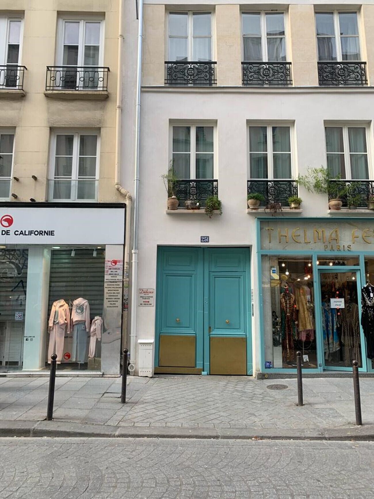 A street view with a boutique store named "THELMA F." and a clothing store named "DE CALIFORNIE" with mannequins displaying outfits.