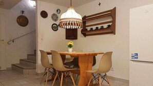 Ein Essbereich mit einem Holztisch, vier Stühlen, einer Hängelampe und einem Wandregal mit Tassen.