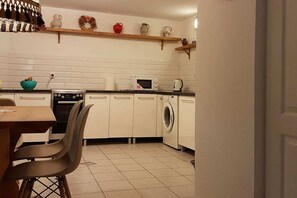Une cuisine avec des meubles blancs, une cuisinière, un four à micro-ondes et un lave-linge.