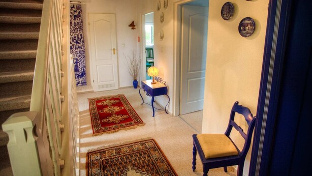 Eine Treppe führt zu einer Zwischenebene mit einem blauen Stuhl und einem Tisch mit einer Lampe.