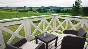 Eine Terrasse mit Korbmöbeln und einem Tisch, mit Blick auf eine grüne Landschaft.