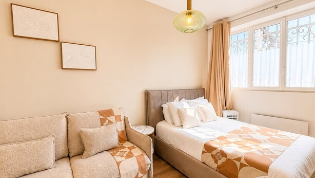 Een slaapkamer met een bed, een bank, een nachtkastje, een lamp en een raam met gordijnen.