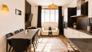 A modern kitchen with a dining area, a sofa, and a TV mounted on the wall.