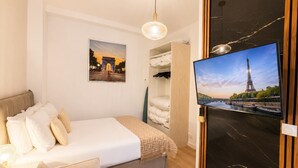 Een slaapkamer met een bed, een televisie, een kledingkast en een afbeelding van de Eiffeltoren.