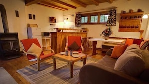 Un salon chaleureux avec un plancher en bois, un canapé, deux fauteuils, une table à manger et un coin cuisine équipé d’un réfrigérateur et d’une cuisinière.