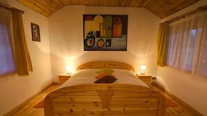 Un lit en bois avec une tête de lit, deux tables de chevet avec des lampes, un tableau au mur et une fenêtre avec des rideaux.