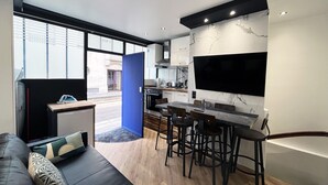 Cozinha moderna com uma televisão grande, área de refeições com banquetas altas e sofá com almofadas estampadas.