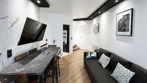Uma sala de estar moderna com uma mesa de jantar de mármore, sofás pretos e uma televisão de tela plana fixada na parede.