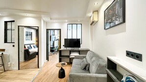 A modern living room with a grey sofa, a coffee table, a TV, and a painting on the wall. - Urban Flat 173 - Atelier Gaite Montparnasse Apartment (París)