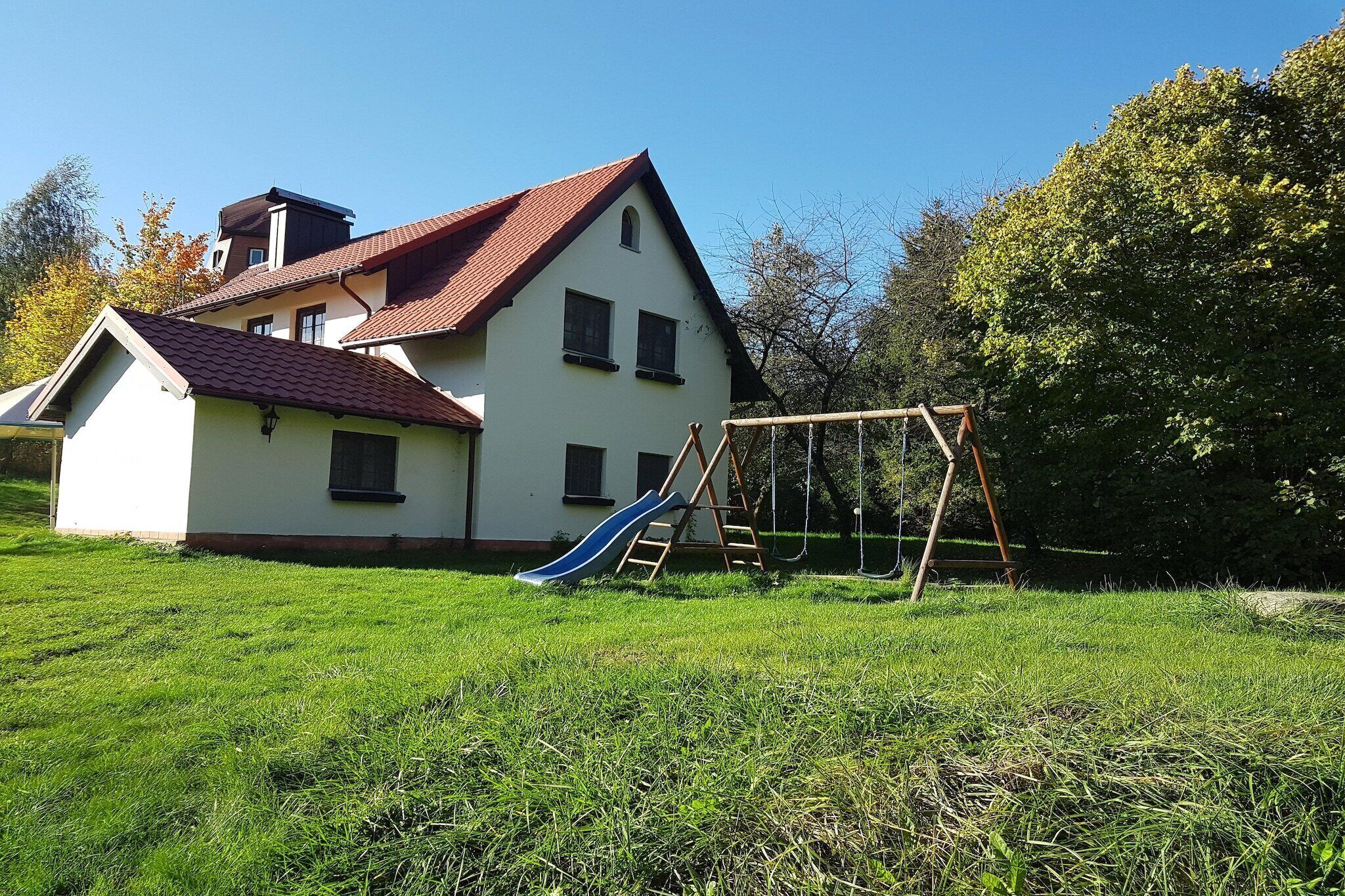 A house with a red-tiled roof, a white exterior, and a blue slide in the yard.