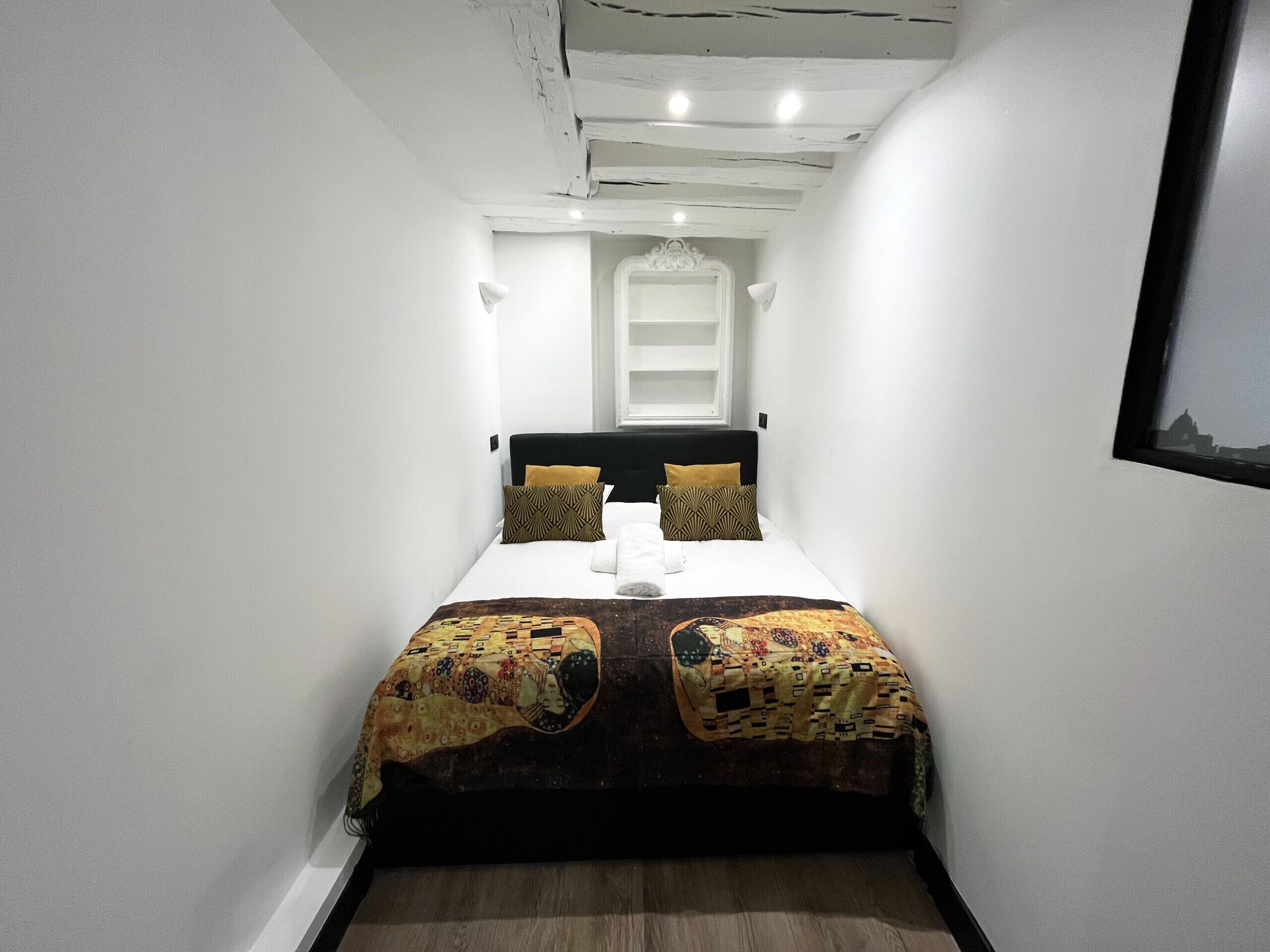 A narrow room with a bed, white walls, and a wooden floor.
