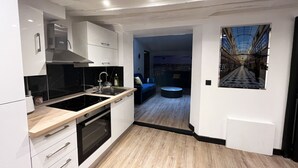Una cocina moderna con armarios blancos, una estufa negra y una encimera de madera. Hay una zona de comedor con un sofá azul y una mesa redonda. Una ventana grande muestra una vista panorámica de la ciudad.