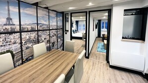 Un moderno cuarto de hotel con un ventanal amplio que ofrece vistas a la ciudad, una mesa de comedor de madera y una zona de estar acogedora.