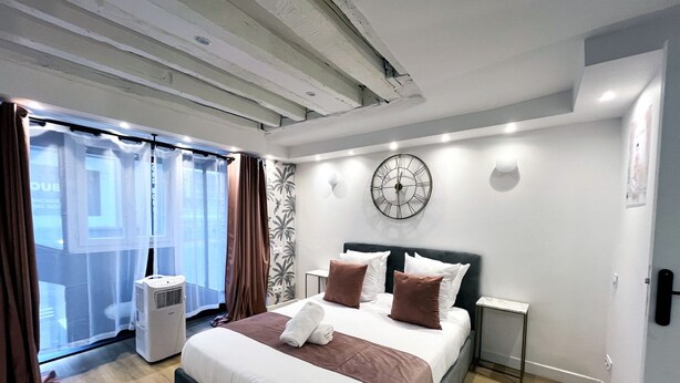 Ein Hotelzimmer mit einem großen Bett, einer Wanduhr, einem Fenster mit Vorhängen und einer Decke mit freiliegenden Balken.