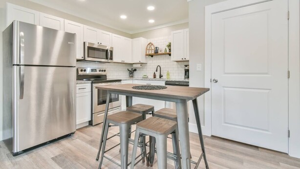 Una cocina moderna con armarios blancos, electrodomésticos de acero inoxidable y una isla central con taburetes.