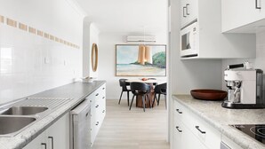 Une cuisine moderne avec des meubles blancs, un four encastré et une machine à café.