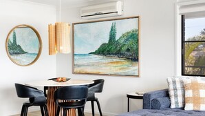 Un salon moderne avec une table de salle à manger ronde, deux chaises noires, un canapé bleu et un grand tableau représentant une plage.