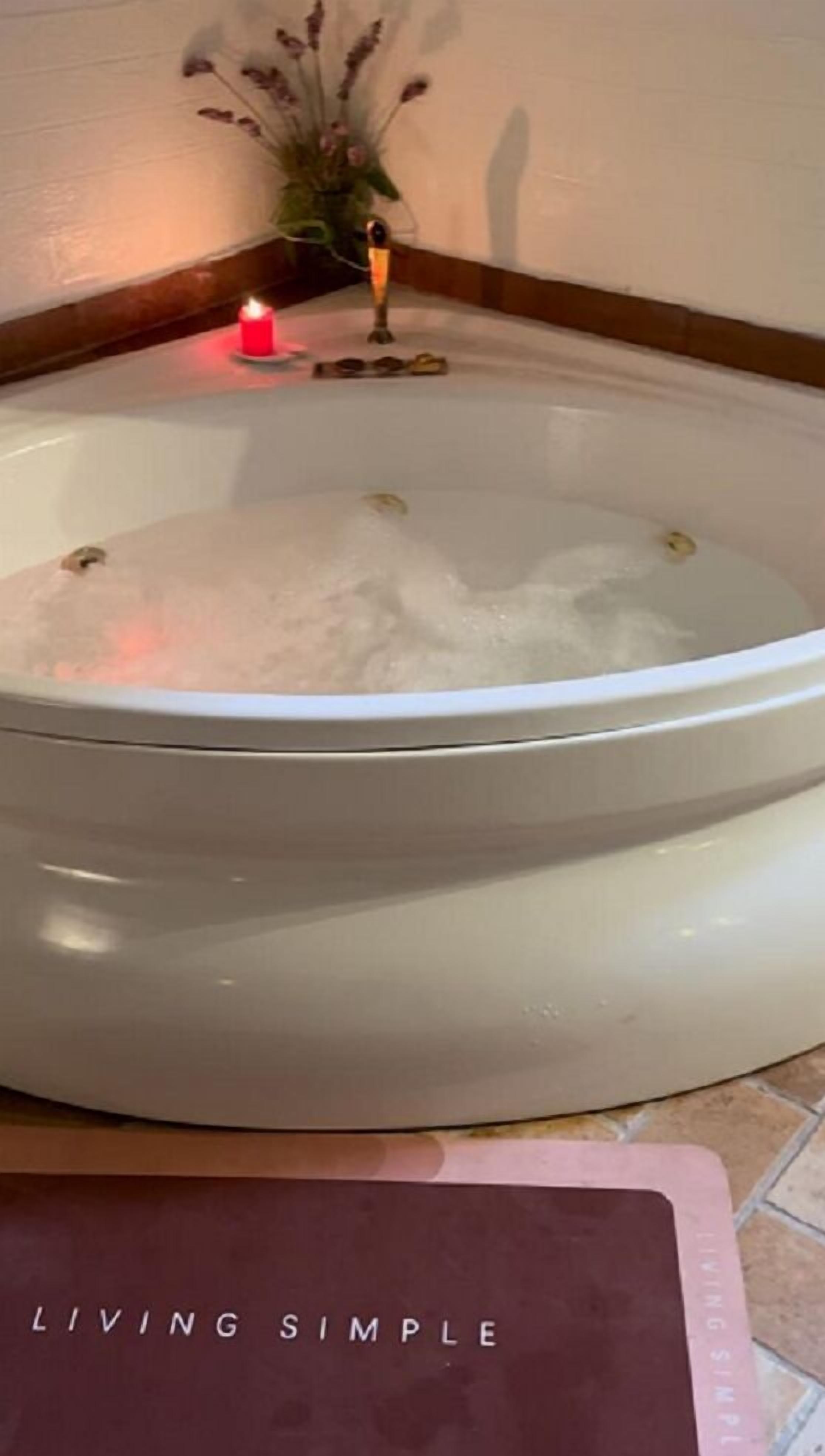 A white bathtub filled with water, a lit candle, and a small plant in the corner.