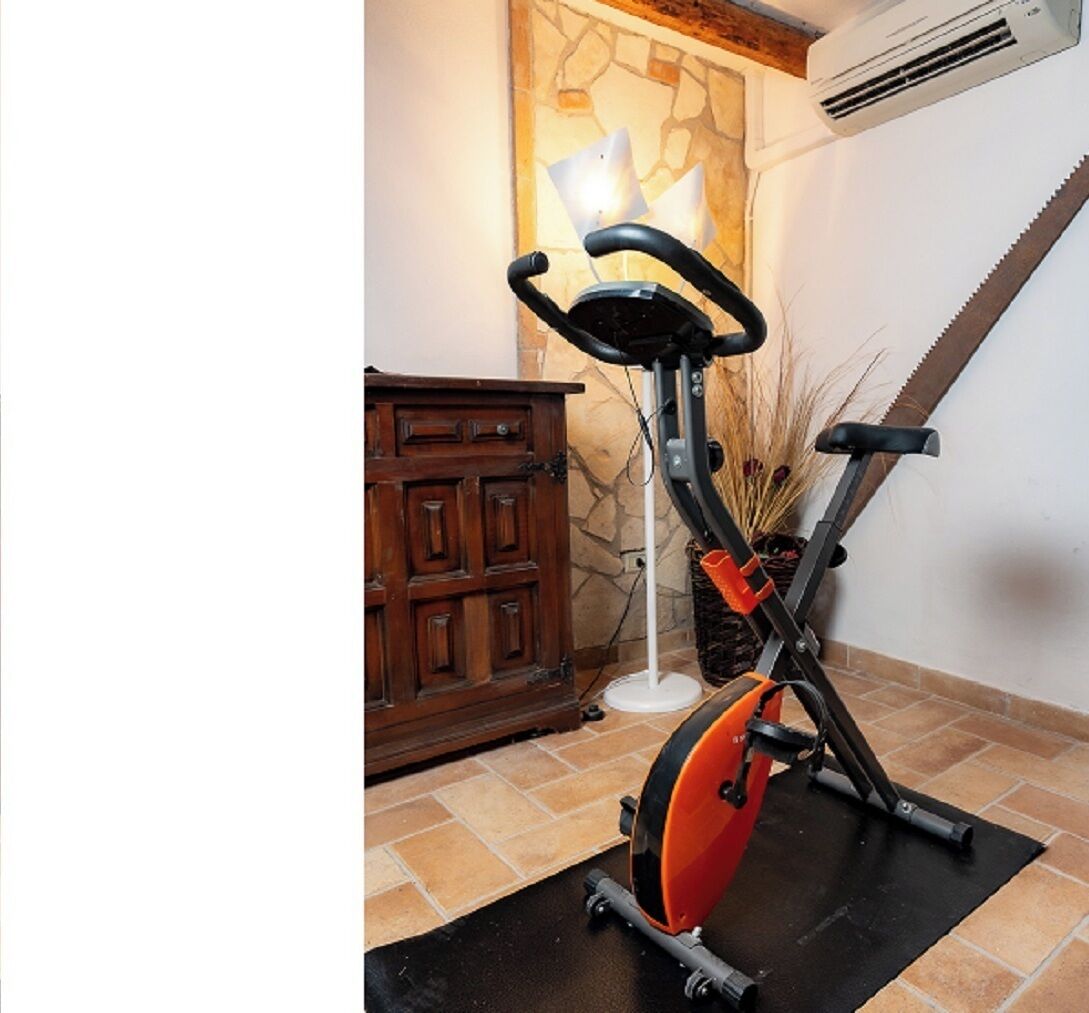 Ein stehendes Fitnessfahrrad in einem Raum mit Steinwand, Holzschrank und Fliesenboden.