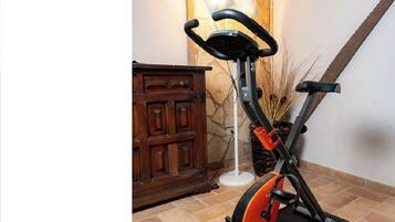 Ein stehendes Fitnessfahrrad in einem Raum mit Steinwand, Holzschrank und Fliesenboden.