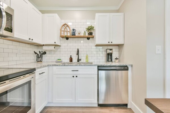 A modern kitchen with white cabinets, a stainless steel dishwasher, and a granite countertop.