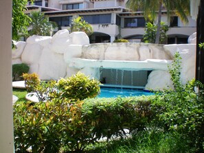 A pool area with a waterfall feature, surrounded by greenery and a building in the background. - Casa Clarita top Location for Your Cancun Experience (Cancún)