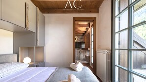 Un dormitorio moderno con un ventanal grande, una cama, una mesita de noche y vista a la cocina.