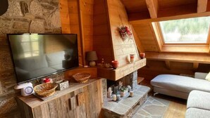 Un acogedor interior de cabaña con una chimenea de piedra, un televisor sobre un soporte de madera y una zona de estar confortable.