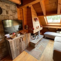 Un acogedor interior de cabaña con una chimenea de piedra, un televisor sobre un soporte de madera y una zona de estar confortable.