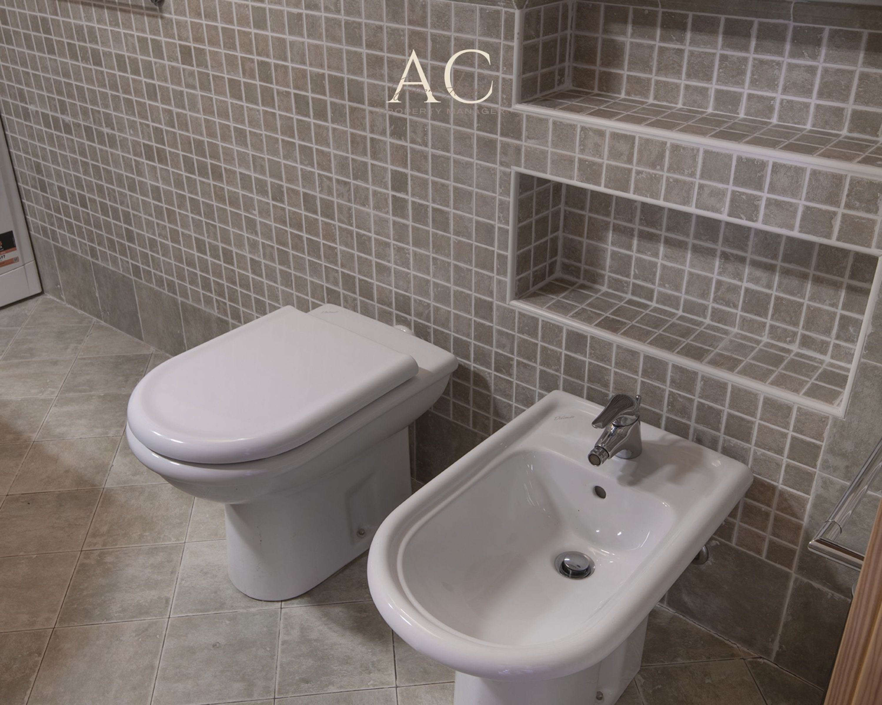 A bathroom with a toilet and bidet, tiled walls, and a tiled floor.