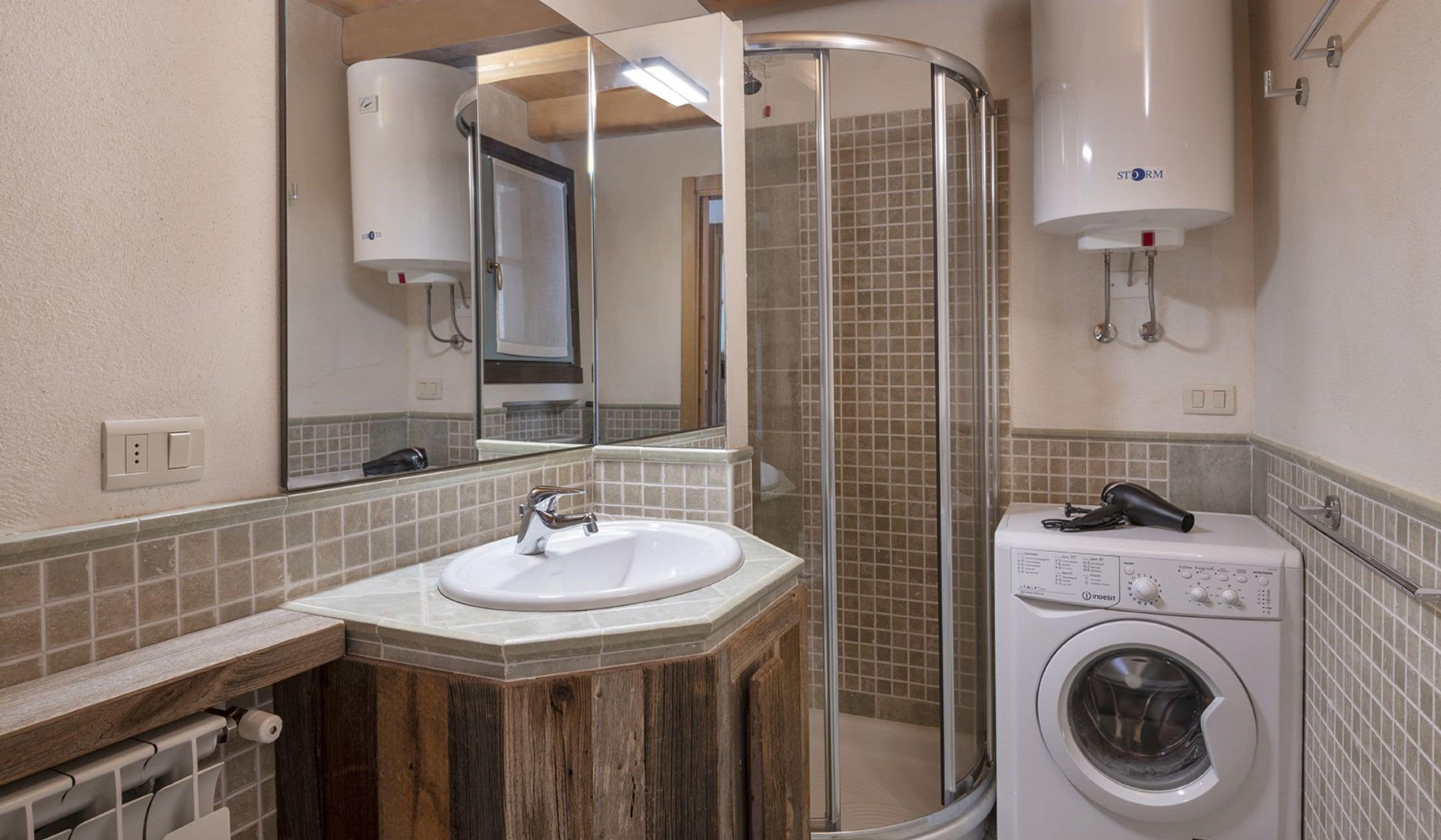 A bathroom with a wooden vanity, a sink, a mirror, a shower enclosure, and a washing machine.