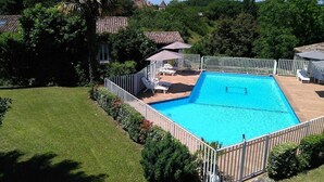 A rectangular swimming pool with a white fence, surrounded by a well-maintained lawn and trees.