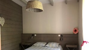 A bedroom with a wooden headboard, a striped bedspread, two bedside tables with lamps, and a woven light fixture.